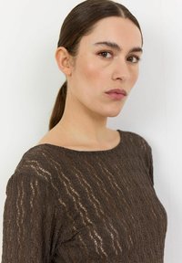 Barna textúrájú blúz, hullámos mintázattal, széles nyakkivágással és hosszú ujjal, könnyű, áttetsző anyagból készült.