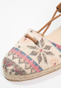 Chaussure espadrille plate avec dessus en tissu tissé présentant des motifs géométriques et floraux colorés et des lacets marron à la cheville.