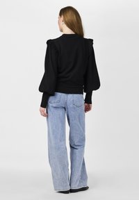 Svart tröja med puffärmar, ribbade handleder och en åtsittande midja; parat med ljusblå vida jeans. Enfärgad bakgrund.