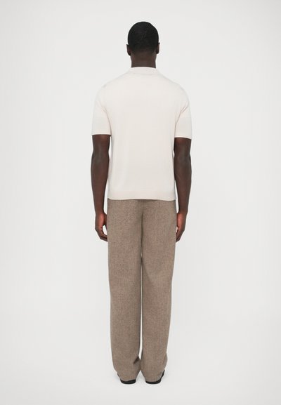 Ανοιχτό μπεζ πόλο μπλουζάκι με κοντά μανίκια, συνδυασμένο με καφέ μάλλινες παντελόνες προσαρμοσμένης γραμμής. Το ύφασμα φαίνεται απαλό με μια διακριτική υφή.
