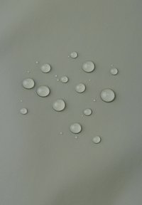 Wassertropfen in verschiedenen Größen auf einem strukturierten, hellgrünen Hintergrund, die klare, glatte Oberflächen und subtile Reflexionen zeigen.
