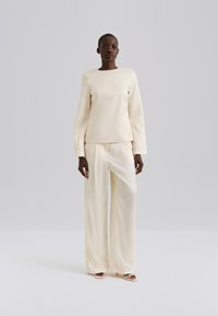 Kremfarget langermet topp med firkantet utringning, kombinert med vide bukser, begge laget av glatt, skinnende stoff. Enkel design, uten mønstre.