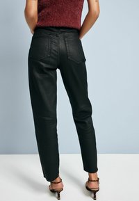 Černé kalhoty s vysokým pasem a slim fit, s zadními kapsami a roztrženými lemy. Materiál má mírný lesk. Pořené s páskovými podpatky.