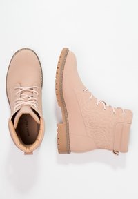 Ljusrosa snörstövlar med floral präggning och en vadderad krage i tan, visade från ovan och sidan på vit bakgrund.