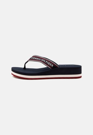 Marineblå kileflip-flop med rød, hvid og marineblå stribet rem med mærket "Tommy Hilfiger" på siden og en rød sål bund.