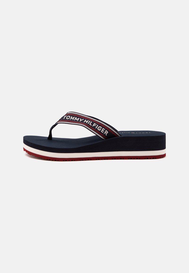 Tong compensée bleu marine avec bride rayée rouge, blanche et bleu marine, marquée "Tommy Hilfiger" sur le côté et semelle rouge.