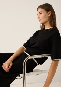 Haut noir en tricot avec un col rond, des manches courtes et des accents blancs sur les bords, assorti à un bas noir assorti. Chaise métallique.