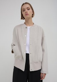 Veste en mélange de laine beige avec un ourlet côtelé, fermeture à pression et coutures courbes. Caractéristiques : coupe décontractée et épaules tombantes.