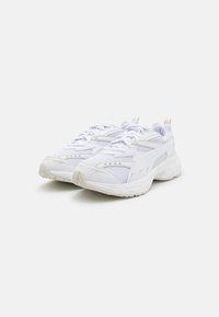 White athletic sneakers with mesh and synthetic material, rounded shape, thick rubber sole, and subtle gray accents on the upper.