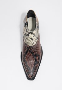 Zapato de punta afilada hecho de piel de serpiente multicolor, con una textura brillante y un patrón en negro y marrón, y con un cierre lateral.