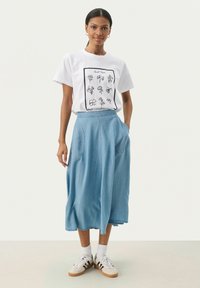 T-shirt alb cu grafică de floare neagră, combinat cu o fustă midi din denim albastru deschis, cu buzunare laterale și o croială relaxată. Adidași albi cu dungi negre.