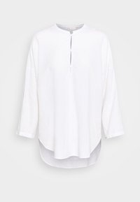 Camicia bianca in lino con scollatura rotonda, mezze bottoni parziali, maniche a tre quarti e orlo posteriore leggermente più lungo. Texture morbida.