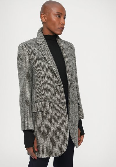 Blazer s uzorkom houndstooth u sivoj i crnoj boji, sa izrezanim ovratnikom, dva prednja džepa i opuštenim krojem. Glatka vunena tekstura.