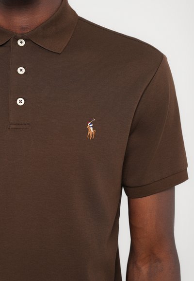 Camisa polo marrón hecha de tejido texturizado, con un cuello tradicional, una tapeta de tres botones y un pequeño logotipo bordado en el pecho.