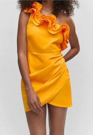 Femme portant une robe jaune vif à une épaule avec des détails volantés le long du décolleté et une jupe portefeuille.