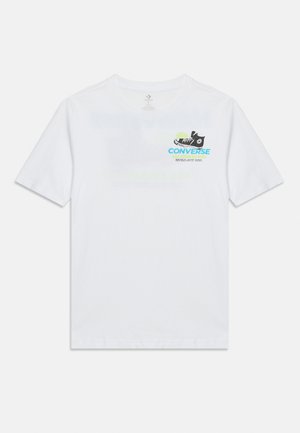 Camiseta blanca de manga corta con un pequeño gráfico de una zapatilla negra Converse y texto azul "CONVERSE" en la parte superior izquierda del pecho.