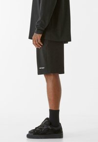 Crna dukserica i šorts s crnim patikama. Šorts ima bijeli logo s natpisom "LOST YOUTH." Materijal izgleda mekano, ležeran dizajn.