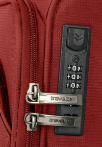Valigia rossa con texture, dotata di tiranti in metallo, con una serratura a combinazione e marchio "travelite" sulla zip e sul meccanismo della serratura.