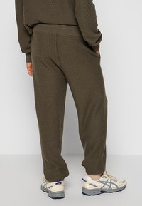 Dunkelolivgrüne Loungehosen mit einem strukturierten Strickmuster, elastischem Bund, Seitentaschen und einer lockeren Passform, kombiniert mit hellen Sneakers.