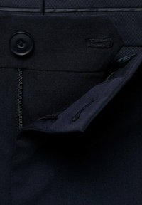 Dunkelblaue Stoffhose mit vorderem Knopfverschluss, sichtbaren Nähten und einer Seitentasche. Das Material wirkt glatt und robust.