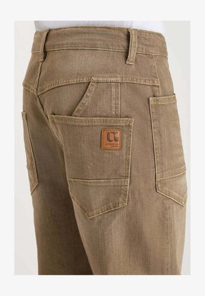 Pantaloni da lavoro marroni con tasche posteriori rinforzate e doppie e un'etichetta in pelle sul bordo della tasca destra.