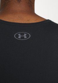 Černé sportovní tričko s hladkým povrchem, má kulatý výstřih a šedé logo na zadní straně poblíž límce.
