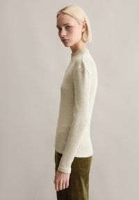 Gerippter, hellbeiger Rollkragenpullover mit langen Ärmeln, taillierter Passform und hohem Kragen. Der Stoff hat eine weiche Textur.