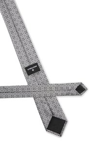 Des bretelles grises à motif géométrique, avec des extrémités en cuir noir et une étiquette de logo. Le matériau semble être un tissu avec une finition texturée.