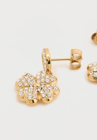 Χρυσά σκουλαρίκια σε σχήμα λουλουδιού, διακοσμημένα με διαυγείς στρας, με πείρο για ασφαλή εφαρμογή. Ομαλή υφή με γυαλιστερό φινίρισμα.