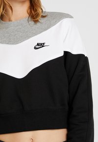 Svart, grå och vit kortärmad tröja med chevrondesign och Nike-logotyp broderad i svart. Tillverkad av ett mjukt, texturerat material.