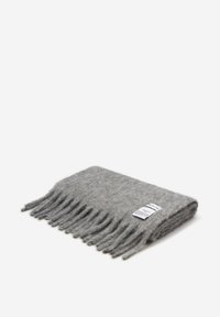 Écharpe en laine grise avec des bords à franges, offrant une texture douce. Comprend une étiquette d'entretien avec un texte noir près du bord. Forme rectangulaire.