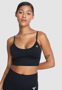 Czarny stanik sportowy z dekoltem w serek, cienkimi ramiączkami i dopasowanym krojem. Zawiera subtelny detal z białym logo po boku.