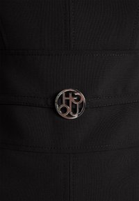 Close-up of silver circular belt buckle with interlocking letters on black fabric garment with visible stitching.