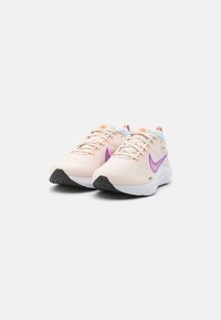 Scarpe sportive color pesco chiaro con accenti viola, progettate con una tomaia in tessuto testurizzato, un'intersuola bianca e una suola in gomma nera.