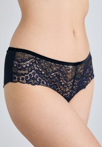 Navy blonde undertøy med en svart stoffbase. Har intrikate blomster mønstre på blonden og en glatt tekstur langs midjebåndet og sidene.