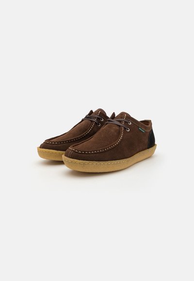 Brown suede shoes with a rounded toe, contrasting black heel accents, brown laces, and tan rubber sole. Visible stitching detail enhances design.