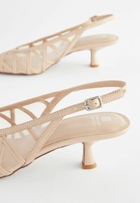Nude slingback hæle med en lav blokhæl. Har et mesh-paneldesign, tynde stropper og en poleret finish. Inkluderer spænde-lukning.