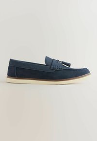 Mocassin en daim bleu marine avec bande texturée tissée et détail pompon, semelle blanche et semelle intermédiaire marron, présenté de profil sur fond neutre.