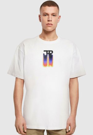 Valkoinen puuvillapaidan, jossa on musta ja gradientti logo "JR" sinisellä, purppuralla ja oranssilla keskellä. Rentoa leikettä ja lyhyet hihat.