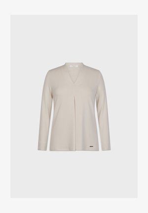 Top beige a maniche lunghe con scollatura a V, caratterizzato da una piega centrale e un piccolo logo metallico vicino all'orlo. Materiale morbido e leggero.