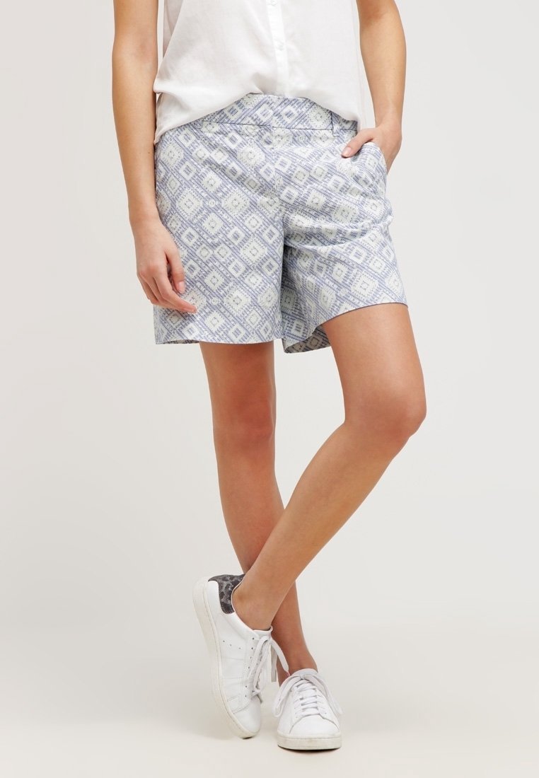 Jasnoniebieskie szorty w wzór diamentów, wyposażone w elastyczny pas. Połączone z białymi trampkami i zapinaną na guziki białą koszulą.