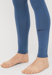 Μπλε αθλητικές κολάν από ελαστικό υλικό. Διαθέτουν εφαρμοστή σχεδίαση, επίπεδες ραφές και μικρό μαύρο λογότυπο Nike στο κάτω μέρος του ποδιού.