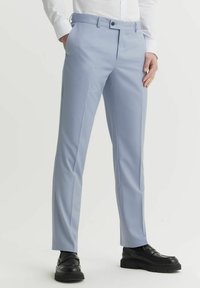 Jasnoniebieskie spodnie wykonane z gładkiego materiału, o dopasowanym kroju, z płaskim przodem i szlufkami na pasek. Połączone z czarnymi butami, prezentując elegancki wygląd.