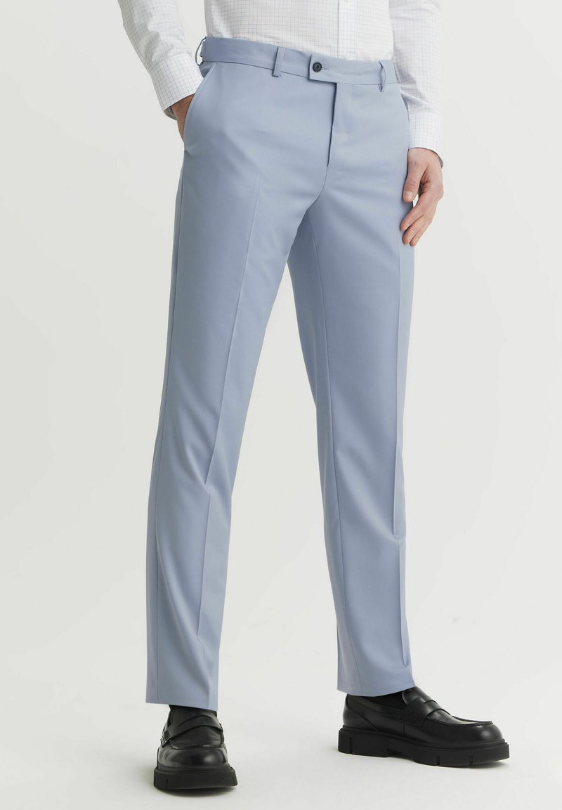 Jasnoniebieskie spodnie wykonane z gładkiego materiału, o dopasowanym kroju, z płaskim przodem i szlufkami na pasek. Połączone z czarnymi butami, prezentując elegancki wygląd.