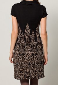 Zwarte jurk met een beige onderkant met patroon, voorzien van ingewikkelde ontwerpen. Korte mouwen en een subtiele kraag maken de look compleet.