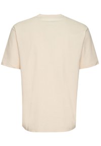 Camiseta de manga corta y cuello redondo en algodón beige claro, con un dobladillo plano y una marca mínima en la parte posterior, con una textura suave y un ajuste relajado.