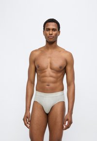 Γκρι βαμβακερά εσώρουχα με λωρίδα λογότυπου Calvin Klein, εφαρμοστή γραμμή, λεία υφή και κλασικό κόψιμο. Το μοντέλο δείχνει το μπροστινό μέρος χωρίς πουκάμισο.