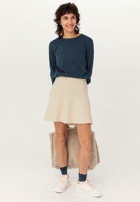 Marineblaues Langarmshirt, beiger gerippter ausgestellter Rock, weiße Sneaker und blaue Socken. Hält eine flauschige beigefarbene Tragetasche. Einfaches und lässiges Design.