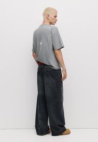 Overdimensioneret grå t-shirt med korte ærmer og lille logo på ryggen, kombineret med brede sorte denimbukser og brune chunky støvler.