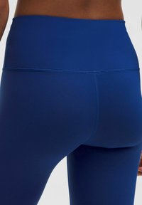 Närbild på en person som bär högmidjade, mörkblå leggings, med fokus på rygg och midja där sömmen är tydligt synlig.